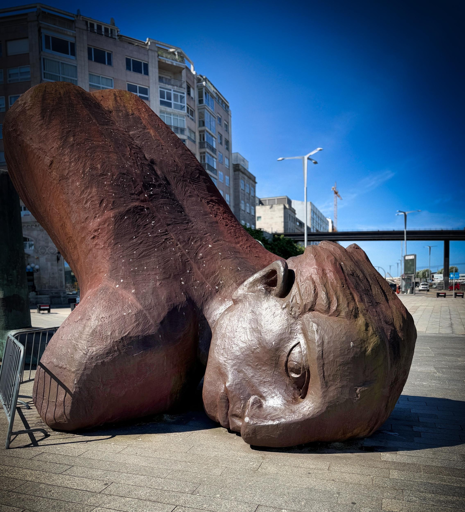 Statua gigante di un volto umano disteso, in un'area urbana sotto un cielo blu brillante.