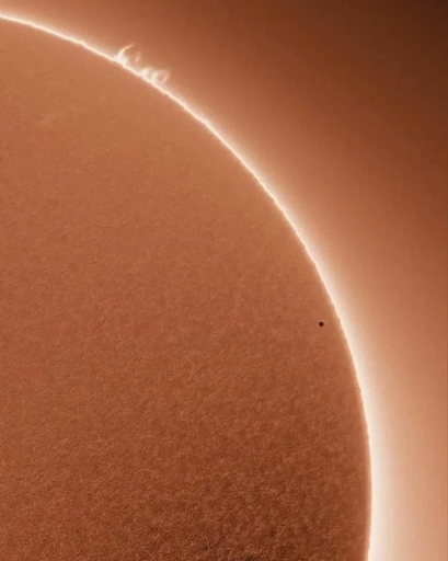 L'immagine mostra un'immagine del Sole, con un bordo luminoso che circonda la sua superficie. La superficie solare appare con una texture granulosa, caratteristica della sua atmosfera. Un piccolo punto nero, che rappresenta Mercurio, è visibile sulla superficie solare, evidenziando un evento solare. La luce solare crea un effetto di sfumatura che va dal bianco al rosso, con un'aura luminosa che circonda il Sole. Questo tipo di immagine è tipico di un'osservazione del Sole durante un evento solare, come un transito o un'annellata solare.