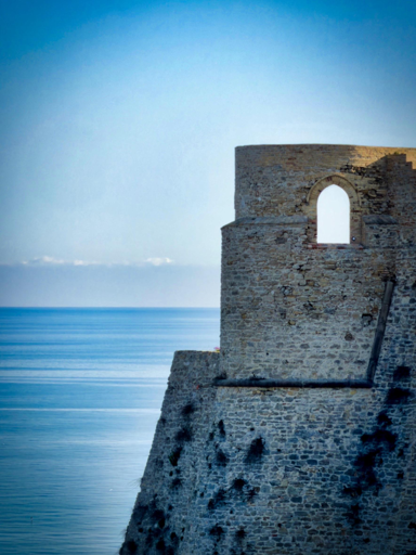 Rudere in pietra sulla scogliera con vista mare e cielo azzurro.