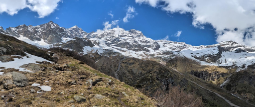 La foto mostra una vista spettacolare del massiccio del Monte Rosa, in particolare della sua imponente parete est, l'unica di dimensioni himalayane delle Alpi.
Un pendio di montagna accidentato, con vegetazione rada e chiazze di neve residua.
Le maestose cime innevate del Monte Rosa, che si stagliano contro un cielo azzurro con nuvole bianche sparse