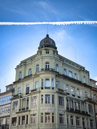 Edificio storico con cupola, balconi e molte finestre, sotto un cielo azzurro con una nuvoletta di condensa.