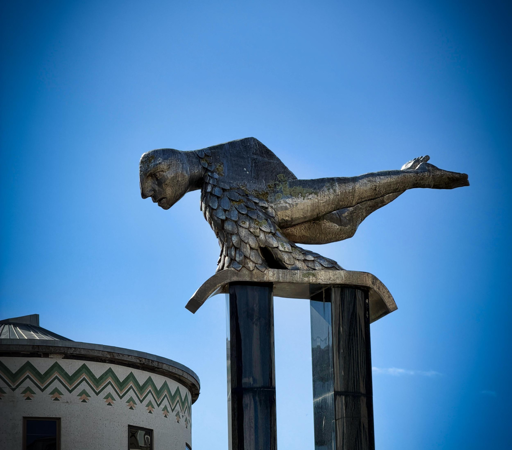 Statua del Sireno , con testa e corpo inclinati verso il basso, sotto un cielo blu - VIGO