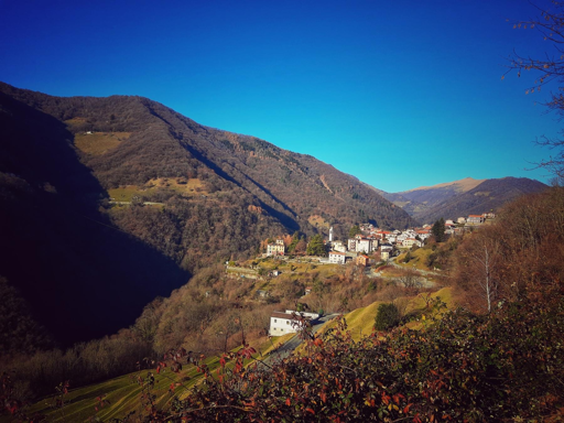 Un piccolo villaggio di montagna è immerso in un paesaggio collinare sotto un cielo azzurro.
