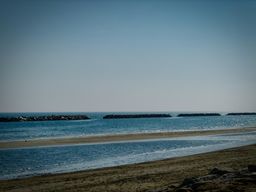 Spiaggia tranquilla con onde calme e scogliere in lontananza sotto un cielo azzurro.