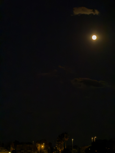 Luna piena nel cielo notturno con nuvole sparse e luci in basso.