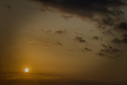 Sole all’alba con cielo nuvoloso in sfumature di arancione e grigio.
