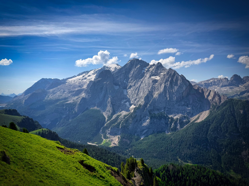 Marmolada con cime innevate e foresta verde sotto un cielo blu con nuvole bianche.