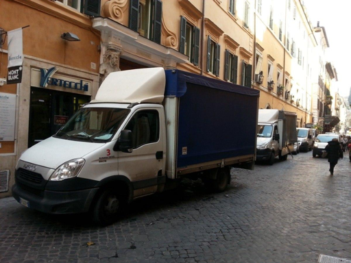 Immagine di un veicolo commerciale impegnato nelle operazioni di carico o scarico delle merci nel centro storico di Roma. Il mezzo si trova in un’area urbana caratterizzata da edifici storici e strade soggette alle regole della ZTL. La fotografia rappresenta il tema della distribuzione delle merci in centro e delle nuove disposizioni che regolano gli orari e le modalità di accesso dei veicoli commerciali.