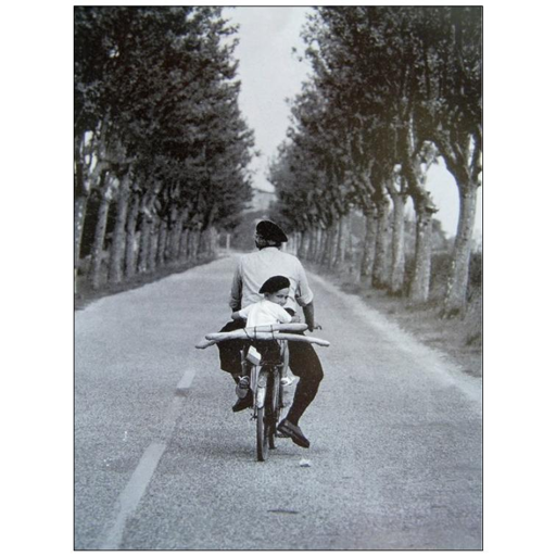 BW of a man driving a bike on a road, with a kid behind his shoulder,s both ones wearing french hats, bringing some baguettes.