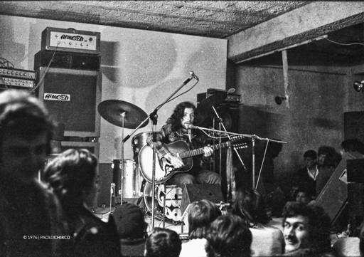 Cantautore alla chitarra su un palco con strumentazione da concerto. Interno del circolo Musica e Cultura a Cinisi nel 1976