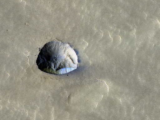 Parte di uno di questi crateri riempiti appare in questa immagine HiRISE e presenta una caratteristica interessante di circa 250 metri (800 piedi) di estensione, vicino al centro dell’immagine.

Ciò che sembra essere stato un piccolo cratere da impatto mostra ora un bordo rettilineo con una scogliera ripida sul lato meridionale. Questa scogliera, esposta verso nord, sembra rivelare materiale ghiacciato simile a quello osservato in altre scarpate rivolte verso i poli che mostrano ghiaccio sepolto in altre regioni del pianeta. Queste scogliere ci offrono una vista “in sezione” del ghiaccio sepolto in quel luogo e possono aiutare a rispondere a domande su com’era il clima marziano quando questo ghiaccio si è formato.