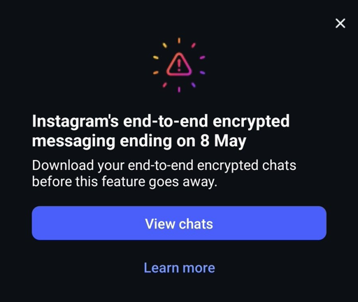 Una schermata di notifica a tema scuro di Instagram che mostra un avviso riguardo a una modifica di una funzionalità. In alto a destra, è presente una piccola icona bianca a forma di "X" per chiudere la notifica. Al centro, sopra il testo, c'è un'icona triangolare colorata che funge da avviso, con un punto esclamativo giallo al suo interno, circondata da piccoli puntini multicolore. Il testo riporta testualmente: "La messaggistica end-to-end crittografata di Instagram terminerà il 8 maggio", seguito da "Scarica le tue chat end-to-end crittografate prima che questa funzionalità venga rimossa." Sotto il testo, un pulsante rettangolare blu con l'etichetta "Visualizza le chat" è posizionato sopra un link blu più piccolo con la dicitura "Scopri di più". Il design generale utilizza uno sfondo nero con elementi di testo bianchi e blu per garantire la chiarezza.


