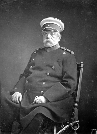 Fotografia in bianco e nero, scattata intorno al 1880, di Bismarck. Seduto su una poltrona, con una giubba militare a doppio petto, un cappello da marina bianco e la spada al fianco, il vecchio ammiraglio ha i suoi folti e celebri baffoni bianchi, l'aria stanca e guarda l'obiettivo con i suoi occhi chiari