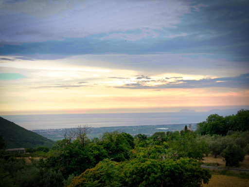 Paesaggio di colline verdi sotto un cielo nuvoloso al tramonto.