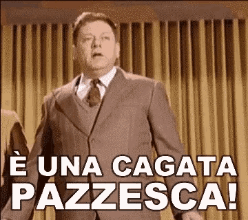  L'immagine mostra un uomo in abito scuro, con una cravatta e una camicia bianca, che cammina verso l'obiettivo con un'espressione di sorpresa o indignazione. Sullo sfondo, si vedono tende verticali di colore marrone chiaro. Sopra l'uomo, in caratteri bianchi e in grassetto, è scritto "È UNA CAGATA PAZZESCA!" Questo testo suggerisce un'emozione intensa, probabilmente di shock o incredulità. L'immagine sembra essere tratta da un film o una serie televisiva, con un'atmosfera vintage.