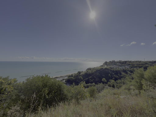 Vista panoramica di mare blu, colline verdi e cielo soleggiato con poche nuvole.