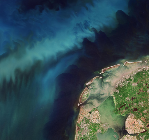 
Questa catena di isole è separata dalla terraferma dalla stretta fascia di acque basse e piane fangose soggette alle maree del Wadden Sea, un’insenatura salmastra del Mare del Nord. Le acque di colore marrone indicano un elevato contenuto di sedimenti, in contrasto con le acque più scure del mare aperto.

Due dighe sono visibili come linee bianche che attraversano le acque interne, creando due distinti bacini d’acqua dolce: il più grande lago IJsselmeer e il più piccolo Markermeer.

Il mosaico di campi agricoli visibile sulle isole e sulla terraferma mostra appezzamenti nelle diverse fasi di crescita o raccolta. Le principali colture dell’area includono cereali, patate, barbabietole da zucchero, cipolle e, naturalmente, tulipani.

Nell’immagine, gli spettacolari campi di tulipani in fiore appaiono in vari colori che vanno dalle tonalità del giallo e del rosso fino al viola. Sebbene duri solo poche settimane, la bellezza di questi colori attira normalmente milioni di visitatori da tutto il mondo. Quando i tulipani raggiungono la piena fioritura, gli agricoltori rimuovono rapidamente le loro colorate corolle per reindirizzare l’energia della pianta verso i bulbi, aiutandoli a mantenersi forti.
