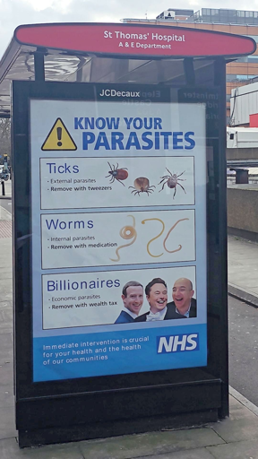 L'immagine mostra un cartellone informativo situato in una fermata di autobus vicino all'ospedale St Thomas' Hospital, in particolare all'A&E Department. Il cartellone, prodotto da JCDecaux, ha un titolo in blu che recita "KNOW YOUR PARASITES" (Conosci i tuoi parassiti) e presenta un avviso giallo con un esclamativo. 

Il cartellone è diviso in tre sezioni:

Parassiti esterni (Ticks): Viene illustrato un parassita esterno, il tartarugone, con l'istruzione di rimuoverlo con pinzette.

Parassiti interni (Worms): Viene illustrato un parassita interno, il verme, con l'istruzione di rimuoverlo con medicazione.

Parassiti economici (Billionaires): Viene illustrato un gruppo di persone con l'istruzione di rimuoverli con un "wealth tax" (tassa sui ricchi).

In basso, c'è un messaggio in blu che recita: "Immediate intervention is crucial for your health and the health of our communities" (L'intervento immediato è cruciale per la tua salute e per la salute delle nostre comunità), con il logo dell'NHS (National Health Service).

Il cartellone è posizionato in una zona urbana, con edifici e un cielo parzialmente nuvoloso visibili sullo sfondo.

