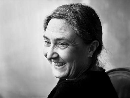 A black and white portrait of a woman smiling softly, wearing a dark sweater. The background is softly blurred, enhancing the focus on her expressive face.