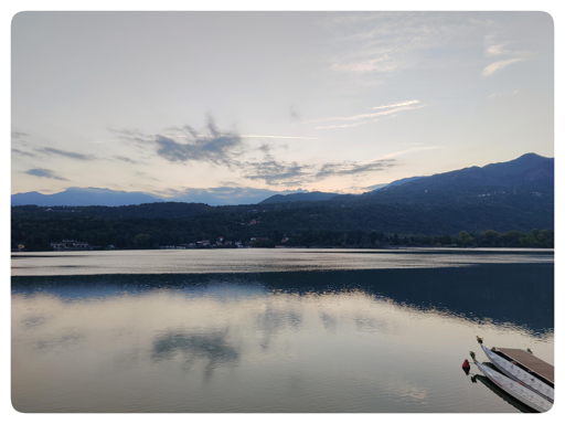 Tramonto sul lago.
L'acqua poco mossa riflette le montagne, il cielo e le nubi. Le montagne sono scure contro il cielo illuminato dall'ultimo sole. Le nubi portano ancora il vago colore caldo del tramonto, mentre si scuriscono in contrasto con il cielo.
Nell'angolo in basso a destra, le due dragonesse.