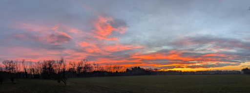 L'immagine mostra un tramonto spettacolare caratterizzato da colori intensi e vibranti che dominano il cielo.
Il cielo è tinto prevalentemente di tonalità calde di rosso, arancione e giallo brillante. Queste sfumature infuocate si concentrano verso l'orizzonte e si mescolano gradualmente con nuvole più scure e grigie nella parte superiore dell'inquadratura. 
I colori osservati durante un tramonto sono determinati dalla lunghezza d'onda della luce che raggiunge l'osservatore dopo aver viaggiato per una maggiore distanza attraverso l'atmosfera rispetto a mezzogiorno, il che spiega lo spostamento verso tonalità più calde. 
